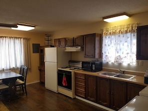 A compact kitchen with a refrigerator, stove, microwave, and wooden cabinets. - The Pines at Mayhill (Mayhill)
