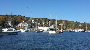 Uma marina com vários barcos atracados, céu claro e um morro com edifícios ao fundo.