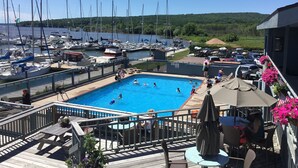 Uma área de piscina com vista para barcos e um cais, rodeada por um deck com mesas e cadeiras.