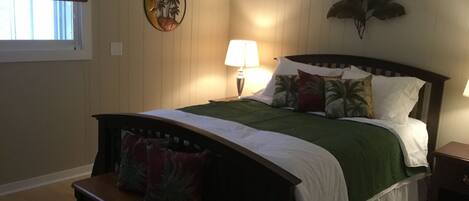 Een slaapkamer met een bed, een nachtkastje, een bankje, een wandklok en een raam met blinds.