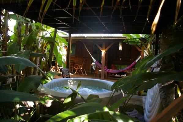 An indoor garden with a hot tub, wooden furniture, and a hammock.