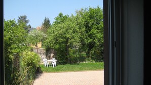 A paved patio with a brick pathway leading to a seating area with white chairs.