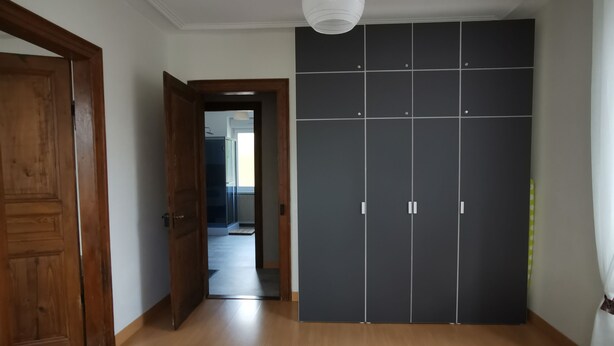 A bedroom with a wooden floor, a grey wardrobe, and a white ceiling light.