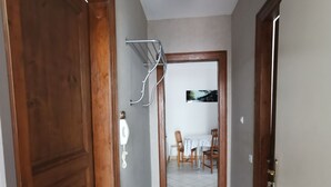 A hallway with wooden doors, a ceiling fan, a coat rack, and a view into a dining area with a table and chairs.