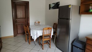 A kitchen with a dining table, chairs, a refrigerator, a trash bin, and a wooden cabinet.