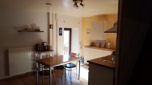 Et lille køkken med spisebord, stole, kaffemaskine, radiator og et ur på væggen.
