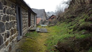 En bygning i sten med et lille haveområde, et metalbord og en træbænk.