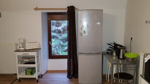 Et lille køkken med et køleskab, kaffemaskine og et vindue med udsigt til grønne områder.