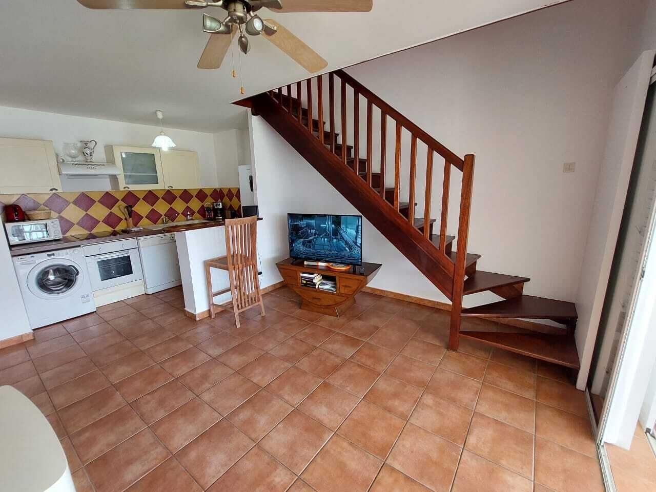 Amplia sala de estar con cocina, una escalera de madera y un televisor de pantalla plana.