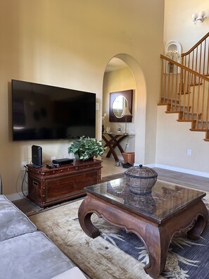 Una sala de estar con televisor de pantalla plana, mueble de madera para entretenimiento y una mesa de centro.