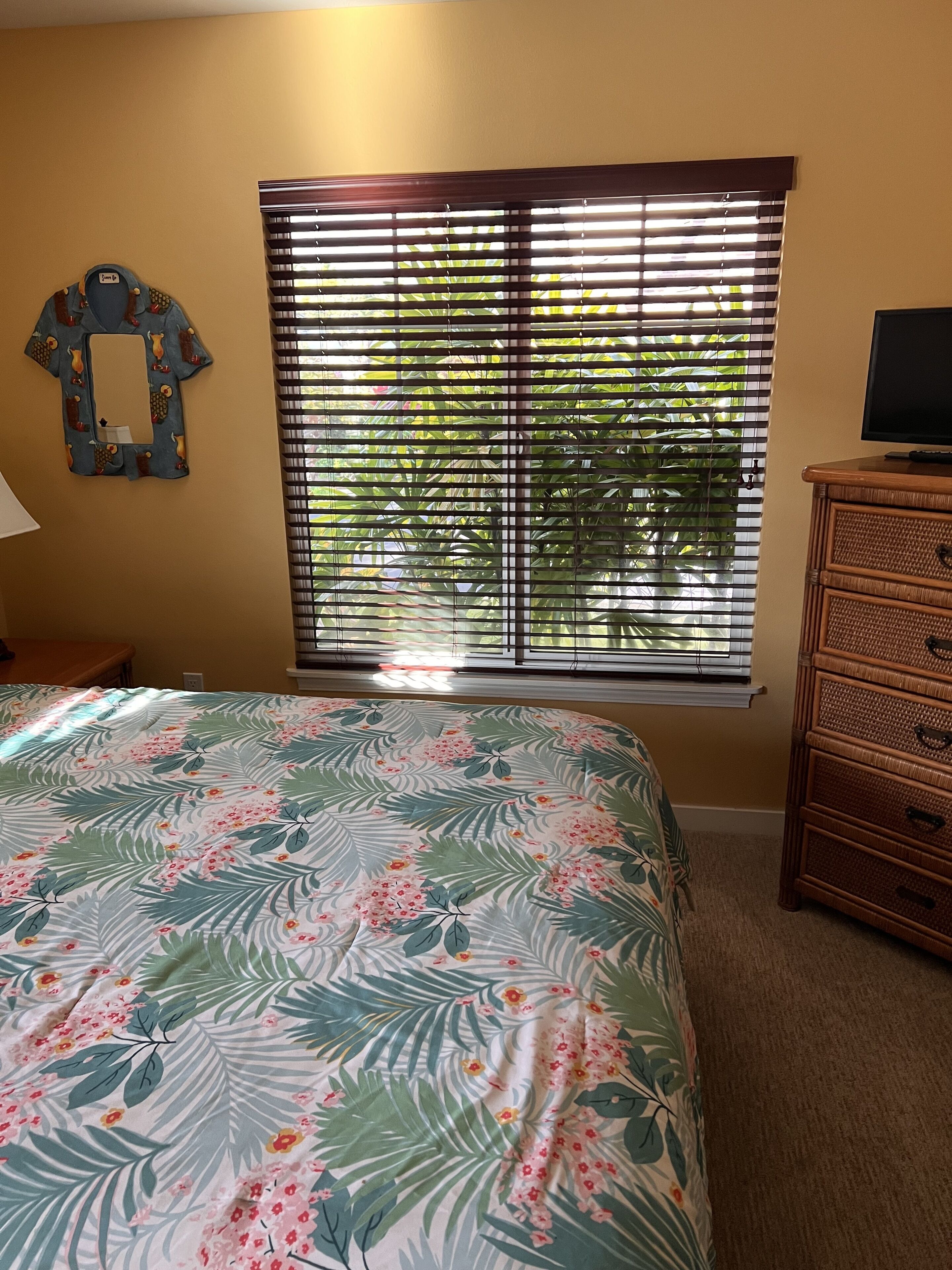 A bedroom with a bed, a dresser, a mirror, and a window with blinds.