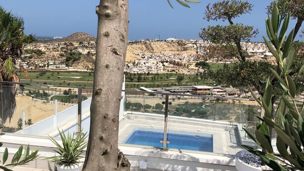 Una terraza en la azotea con piscina, plantas en macetas y vistas a un pueblo en la colina.