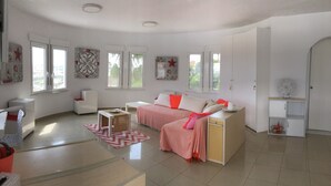 Amplia sala de estar con un sofá, una mesa de centro y un televisor. Hay ventanas, una lámpara de techo y una puerta.