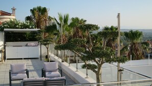Una terraza en la azotea con zona de estar, barandilla de cristal y vistas a la ciudad.