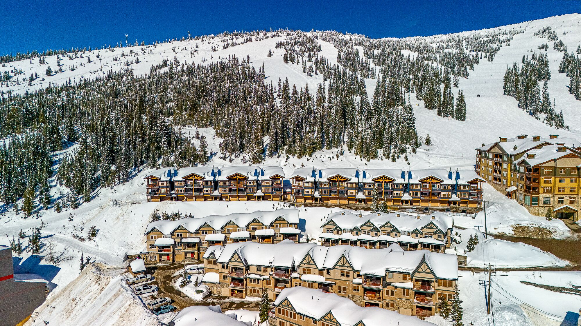 Un albergue cubierto de nieve con varios pisos, telesillas y una pista de esquí al fondo.