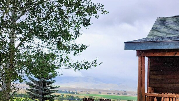 A rustic wooden cabin with a picnic table and chairs, overlooking a vast landscape with fields and distant hills. - Elk Ridge cabin with great views near Yellowstone (Livingston)