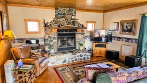 A cozy living room with a stone fireplace, leather sofa, and wooden flooring. - Elk Ridge cabin with great views near Yellowstone (Livingston)