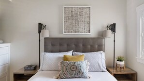 A neatly arranged bedroom with a tufted headboard, a bed with patterned pillows, bedside lamps, and a wall-mounted artwork. - Playa One Bedroom (253) (Carpinteria)