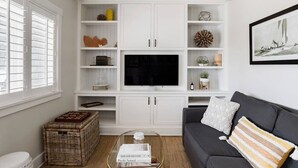 A living room with a large flat-screen TV, white cabinetry, wicker baskets, a gray sofa, and a framed picture on the wall. - Playa One Bedroom (253) (Carpinteria)
