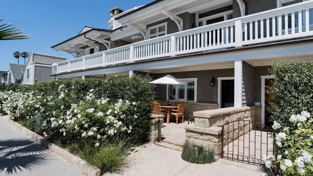 A two-story house with a balcony, a patio with a table and chairs, and white flowering bushes. - Playa One Bedroom (253) (Carpinteria)