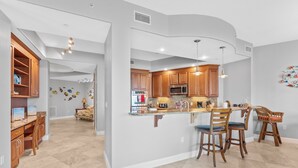 A spacious kitchen with wooden cabinets, a central island with bar stools, and a microwave. - Modern Penthouse with Direct Ocean Front Views! (Cocoa Beach)