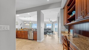 A spacious kitchen with granite countertops, wooden cabinets, and a dishwasher. There is a dining area with a table and chairs, and a view of the sky through large windows. - Modern Penthouse with Direct Ocean Front Views! (Cocoa Beach)