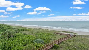 A coastal view with a wooden boardwalk leading to the beach, surrounded by lush greenery. - Modern Penthouse with Direct Ocean Front Views! (Cocoa Beach)