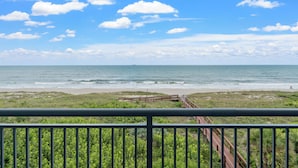 A beach view with a wooden walkway leading to the shore, surrounded by greenery. - Modern Penthouse with Direct Ocean Front Views! (Cocoa Beach)