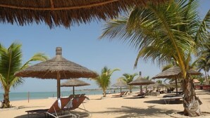 A beach with thatched umbrellas and palm trees, providing shade and a tropical setting.