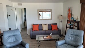 Een woonkamer met een grijze bank, twee blauwe fauteuils, een salontafel en een spiegel boven de bank.