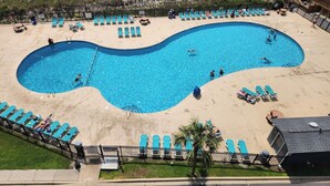 A swimming pool with a unique shape, surrounded by beach chairs and umbrellas, with a beach and ocean in the background. - 50 gas discount applied to rates for weeks in August! Clean condo-sandy beach (Myrtle Beach)