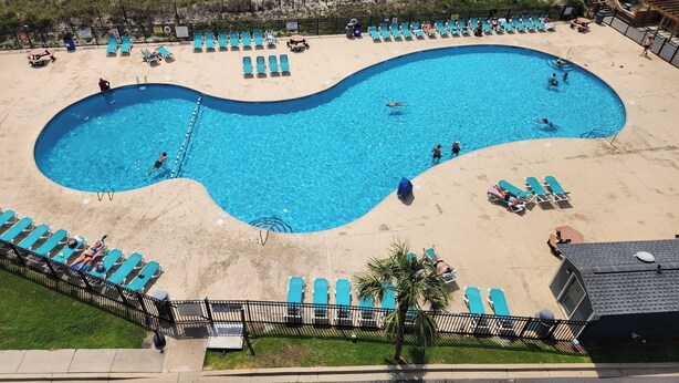 Ein Pool mit ungewöhnlicher Form, umgeben von Liegestühlen und Sonnenschirmen, mit Strand und Meer im Hintergrund.
