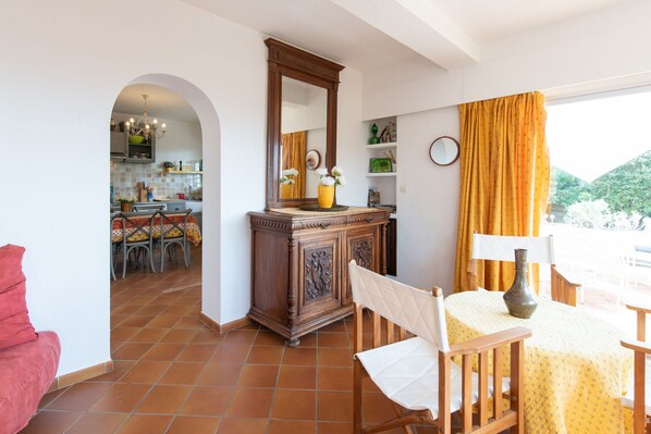 A dining area with a table, chairs, and a mirror. There is a kitchen visible through an archway.