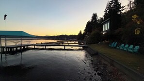 A waterfront area with a covered dock, seating, and a building with large windows.