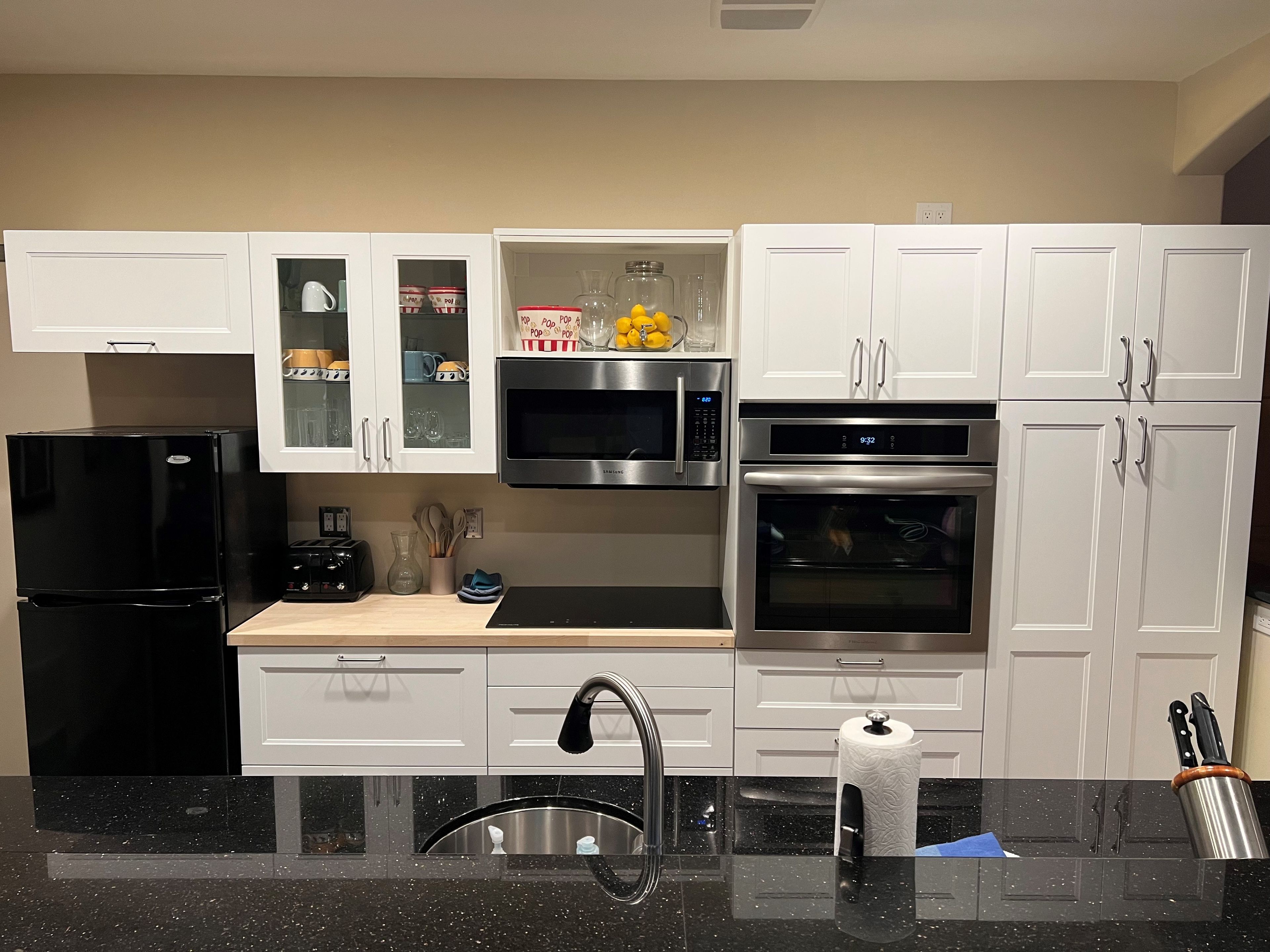A modern kitchen with white cabinets, a black refrigerator, stainless steel appliances, and a black speckled countertop.