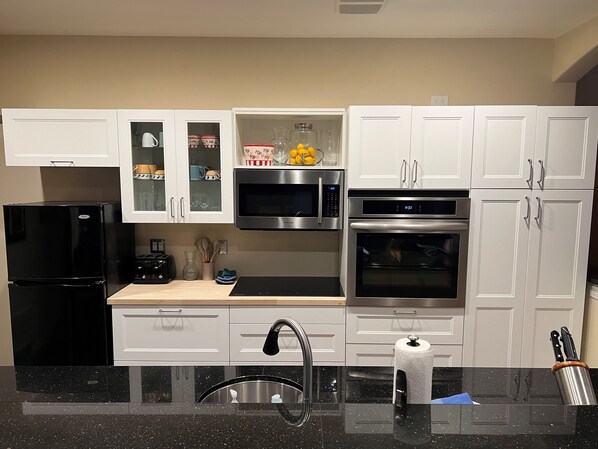 A modern kitchen with white cabinets, a black refrigerator, stainless steel appliances, and a black speckled countertop.
