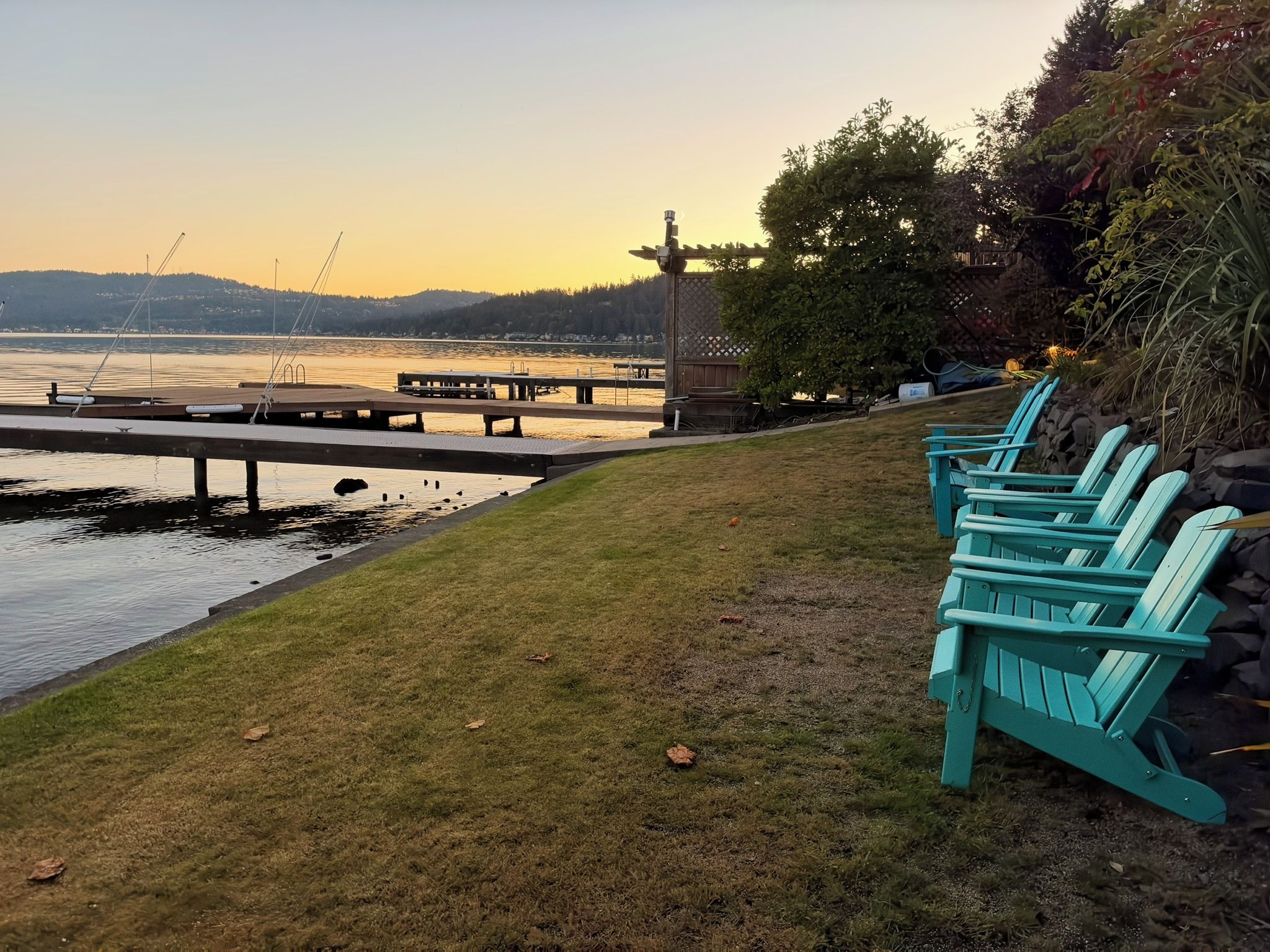 A waterfront view with a dock, chairs, and a grassy area.
