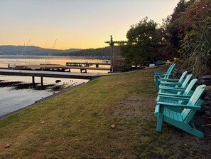 A waterfront view with a dock, chairs, and a grassy area.