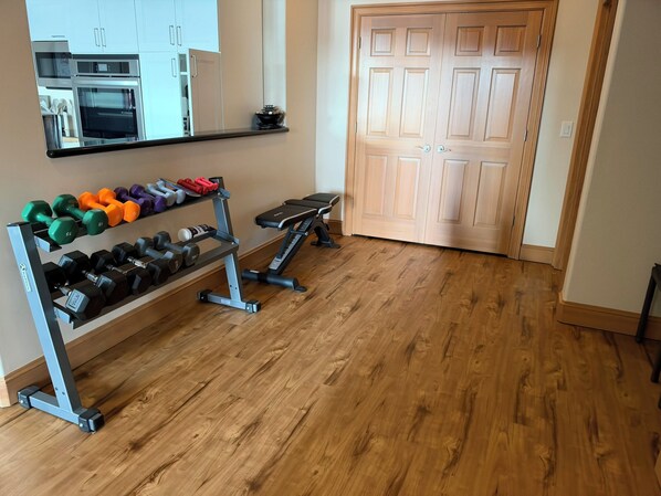 A home gym with a bench, dumbbells, and a rack of weights.