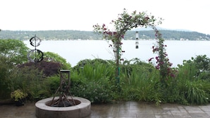 A garden with a circular stone planter, a metal sculpture, and a rose archway overlooking a lake. - 3 bed Lake Sammamish Waterfront + Peloton Bike (Bellevue)