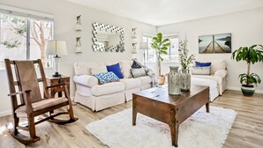 Un salon avec un canapé blanc, un fauteuil à bascule en bois, une table basse et une plante en pot.