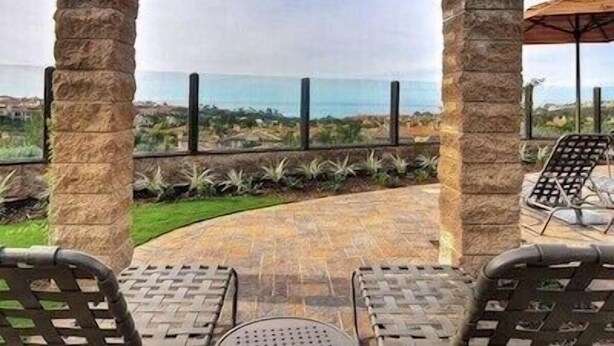 Une terrasse couverte avec des piliers en pierre, deux chaises en métal et une table.