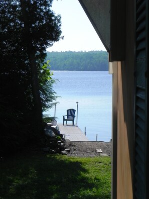 A view from a house to a lake with a dock, a chair, and a lamp post.