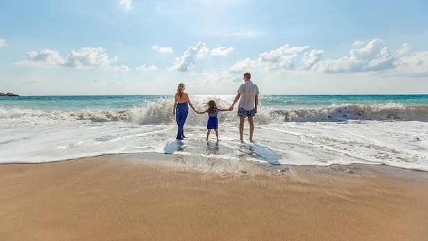Una famiglia che si tiene per mano su una spiaggia sabbiosa, con onde e cielo sereno.