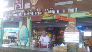 Un bar con diverse bottiglie di liquori, un cartello con scritto Corona Extra e una lavagna dei menu.