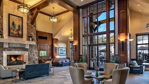 A spacious lobby with a stone fireplace, comfortable seating, and large windows offering views of the outdoors. - Spacious Luxury Two-Bedroom at Grand Lodge at Peak 7! (Breckenridge)