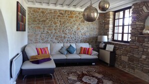 Una sala de estar con una pared de piedra, un sofá con cojines, una alfombra estampada y una ventana con vistas.