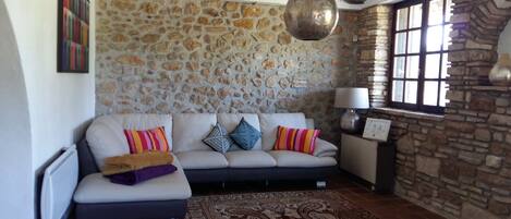 A living room with a stone wall, a sofa with cushions, a patterned rug, and a window with a view.