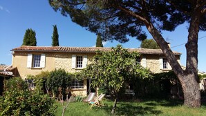 Una casa de piedra de dos plantas con tejado de tejas, rodeada de vegetación y un pequeño jardín con dos sillones.
