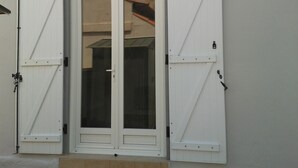 A white door with glass panels, flanked by two white shutters, and a wall-mounted light fixture above. - House for 6 pers. very close to the sea and shops (Agde)